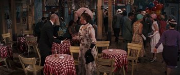 Movie still from “Anastasia” (1956), directed by Anatole Litvak – An older woman in a dress and hat standing in front of a table; Wide shot, Over the shoulder angle