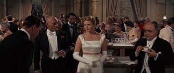 Movie still from “Anastasia” (1956), directed by Anatole Litvak – A woman in a white dress standing in front of a group of people; Medium shot, Over the shoulder angle