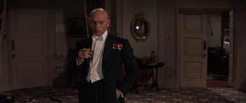 Movie still from “Anastasia” (1956), directed by Anatole Litvak – A man in a suit and bow tie smoking a cigarette; Medium shot, Low angle