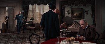Movie still from “Anastasia” (1956), directed by Anatole Litvak – A man standing in a living room next to a table; Wide shot, High angle