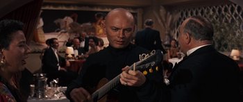 Movie still from “Anastasia” (1956), directed by Anatole Litvak – A bald man in a black shirt is playing a guitar; Close Up shot, Over the shoulder angle