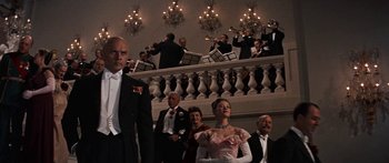 Movie still from “Anastasia” (1956), directed by Anatole Litvak – A group of people in formal wear standing next to each other in front of an orchestra; Medium shot, Low angle