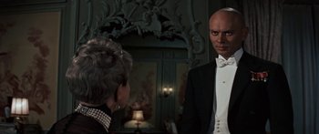 Movie still from “Anastasia” (1956), directed by Anatole Litvak – A man in a tuxedo standing next to a woman in a black dress; Medium shot, Over the shoulder angle
