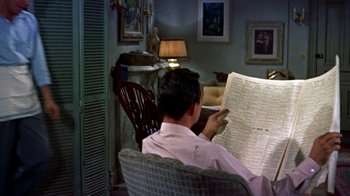 Movie still from “Artists and Models” (1955), directed by Frank Tashlin – A man sitting in a chair reading a newspaper; Medium shot, High angle
