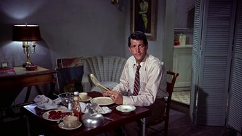 Movie still from “Artists and Models” (1955), directed by Frank Tashlin – A man sitting at a dinner table holding a fork; Medium shot, High angle