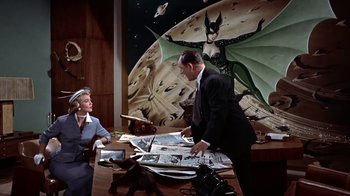 Movie still from “Artists and Models” (1955), directed by Frank Tashlin – A man and a woman in a suit and tie in front of a desk; Wide shot, High angle