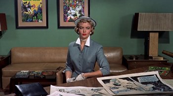 Movie still from “Artists and Models” (1955), directed by Frank Tashlin – A woman sitting at a table in front of pictures; Medium shot, Low angle