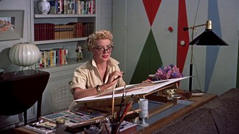 Movie still from “Artists and Models” (1955), directed by Frank Tashlin – An older woman sitting at a table with a painting; Medium shot, Low angle