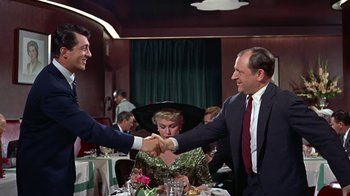 Movie still from “Artists and Models” (1955), directed by Frank Tashlin – Two men shaking hands over a table at a restaurant; Medium shot, Over the shoulder angle