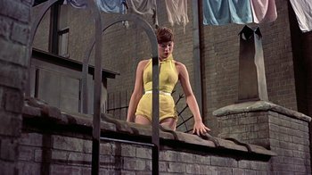 Movie still from “Artists and Models” (1955), directed by Frank Tashlin – A woman in a yellow bathing suit leaning on a brick wall; Medium shot, Low angle