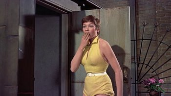Movie still from “Artists and Models” (1955), directed by Frank Tashlin – A woman in a yellow dress standing next to a door; Medium shot, Low angle
