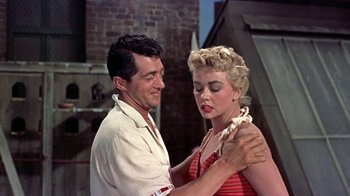 Movie still from “Artists and Models” (1955), directed by Frank Tashlin – A man and a woman are holding each other in front of a brick wall; Medium shot, Low angle