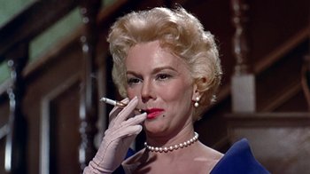 Movie still from “Artists and Models” (1955), directed by Frank Tashlin – An older woman smoking a cigarette while wearing gloves and pearls; Close Up shot, Low angle