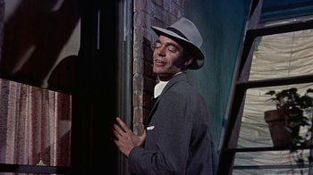Movie still from “Artists and Models” (1955), directed by Frank Tashlin – A man wearing a hat standing next to a brick wall; Medium shot, Low angle