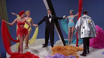 Movie still from “Artists and Models” (1955), directed by Frank Tashlin – A man in a suit standing in front of a group of women; Wide shot, Low angle