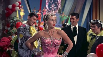 Movie still from “Artists and Models” (1955), directed by Frank Tashlin – A woman in a pink dress standing in front of two other men; Medium shot, Low angle