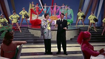 Movie still from “Artists and Models” (1955), directed by Frank Tashlin – A couple of men standing next to each other on a stage; Medium shot, Low angle
