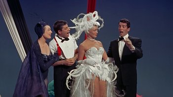 Movie still from “Artists and Models” (1955), directed by Frank Tashlin – A group of people standing around a woman in a white dress; Medium shot, Low angle