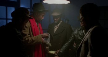 Movie still from “Babylon” (1980), directed by Franco Rosso – A group of men standing around each other in a room; Medium shot, Over the shoulder angle