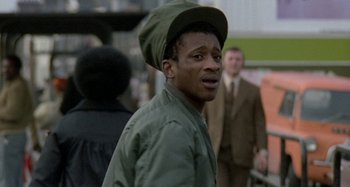 Movie still from “Babylon” (1980), directed by Franco Rosso – A man in a green hat is standing in a crowd; Close Up shot, Over the shoulder angle