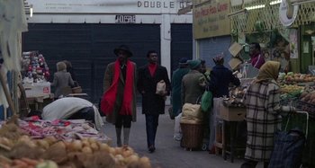 Movie still from “Babylon” (1980), directed by Franco Rosso – A couple of people walking down a street; Wide shot, High angle
