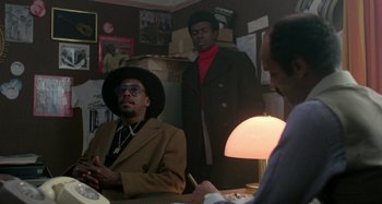 Movie still from “Babylon” (1980), directed by Franco Rosso – A group of men standing around a table; Medium shot, Low angle