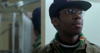 Movie still from “Babylon” (1980), directed by Franco Rosso – A young man wearing glasses and a hat; Close Up shot, Over the shoulder angle