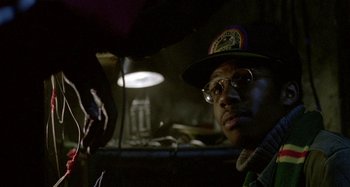 Movie still from “Babylon” (1980), directed by Franco Rosso – A man with glasses and a hat looking at the camera; Close Up shot, Over the shoulder angle