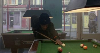 Movie still from “Babylon” (1980), directed by Franco Rosso – A man in a hat playing a game of billiards; Medium shot, High angle