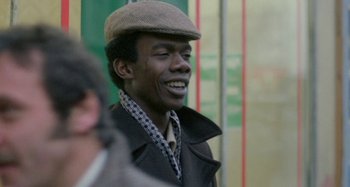 Movie still from “Babylon” (1980), directed by Franco Rosso – A man in a hat and a jacket smiling for the camera; Close Up shot, Over the shoulder angle