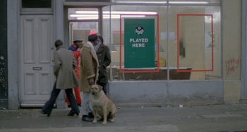 Movie still from “Babylon” (1980), directed by Franco Rosso – A group of people walking down a street with a dog; Wide shot, High angle