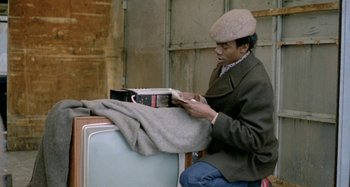 Movie still from “Babylon” (1980), directed by Franco Rosso – A man sitting on top of an old refrigerator; Medium shot, High angle