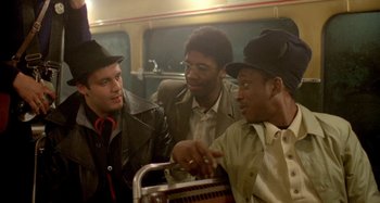 Movie still from “Babylon” (1980), directed by Franco Rosso – A group of men sitting next to each other on top of a train; Medium shot, Over the shoulder angle