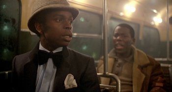 Movie still from “Babylon” (1980), directed by Franco Rosso – A man wearing a suit and a hat riding a bus; Close Up shot, Over the shoulder angle
