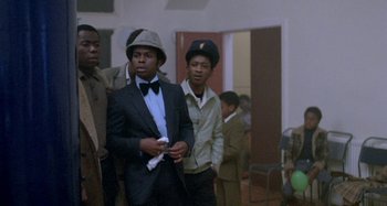 Movie still from “Babylon” (1980), directed by Franco Rosso – A group of young men standing next to each other in a room; Medium shot, Over the shoulder angle