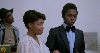 Movie still from “Babylon” (1980), directed by Franco Rosso – A man and a woman standing next to each other in front of a white wall; Close Up shot, Low angle