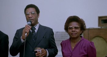 Movie still from “Babylon” (1980), directed by Franco Rosso – A man and a woman standing next to each other holding microphones; Medium shot, Low angle