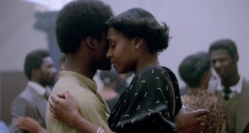 Movie still from “Babylon” (1980), directed by Franco Rosso – A man and a woman embracing each other in front of a crowd of onlookers; Close Up shot, Over the shoulder angle
