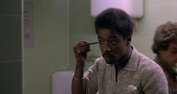 Movie still from “Babylon” (1980), directed by Franco Rosso – A man with a beard is holding a pen in his hand; Close Up shot, High angle