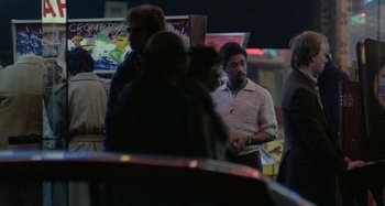 Movie still from “Babylon” (1980), directed by Franco Rosso – A group of people standing around in a room at night; Medium shot, Over the shoulder angle