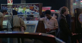 Movie still from “Babylon” (1980), directed by Franco Rosso – A man standing in front of an arcade machine; Medium shot, Over the shoulder angle