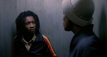 Movie still from “Babylon” (1980), directed by Franco Rosso – Two men talking to each other in front of a gray wall; Medium shot, Over the shoulder angle