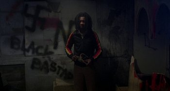 Movie still from “Babylon” (1980), directed by Franco Rosso – A man with dreadlocks standing in front of a wall; Medium shot, Low angle