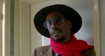Movie still from “Babylon” (1980), directed by Franco Rosso – A man wearing a hat and a red scarf; Close Up shot, Low angle