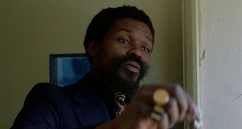 Movie still from “Babylon” (1980), directed by Franco Rosso – A man in a suit and tie holding a watch in his hand; Close Up shot, Low angle