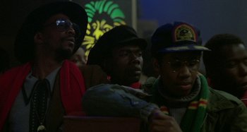 Movie still from “Babylon” (1980), directed by Franco Rosso – A group of men sitting next to each other on a stage; Close Up shot, Low angle