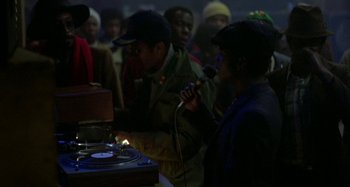Movie still from “Babylon” (1980), directed by Franco Rosso – A group of people standing around a microphone; Medium shot, High angle
