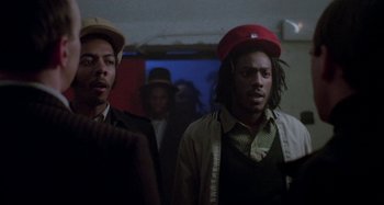 Movie still from “Babylon” (1980), directed by Franco Rosso – A couple of men standing next to each other in a room; Medium shot, Low angle