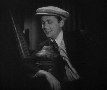 Movie still from “Bad Girl” (1931), directed by Frank Borzage – A man in a suit and hat holding a fire hydrant; Medium shot, High angle