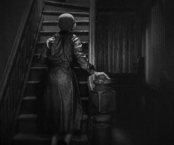 Movie still from “Bad Girl” (1931), directed by Frank Borzage – A woman in a long dress is walking up the stairs with luggage; Medium shot, Low angle